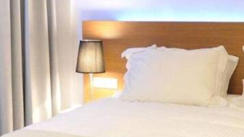 Quarto de hotel com uma cama grande, uma luminária de cabeceira e vista para o céu.
