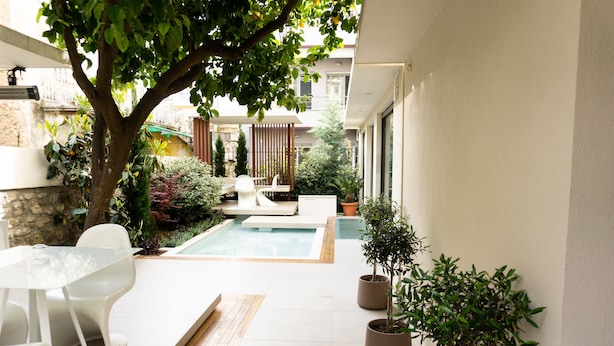 Un patio moderno al aire libre con piscina, mobiliario blanco y plantas en macetas.