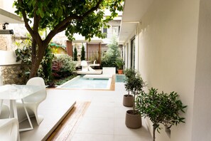 Un patio moderno al aire libre con piscina, mobiliario blanco y plantas en macetas.