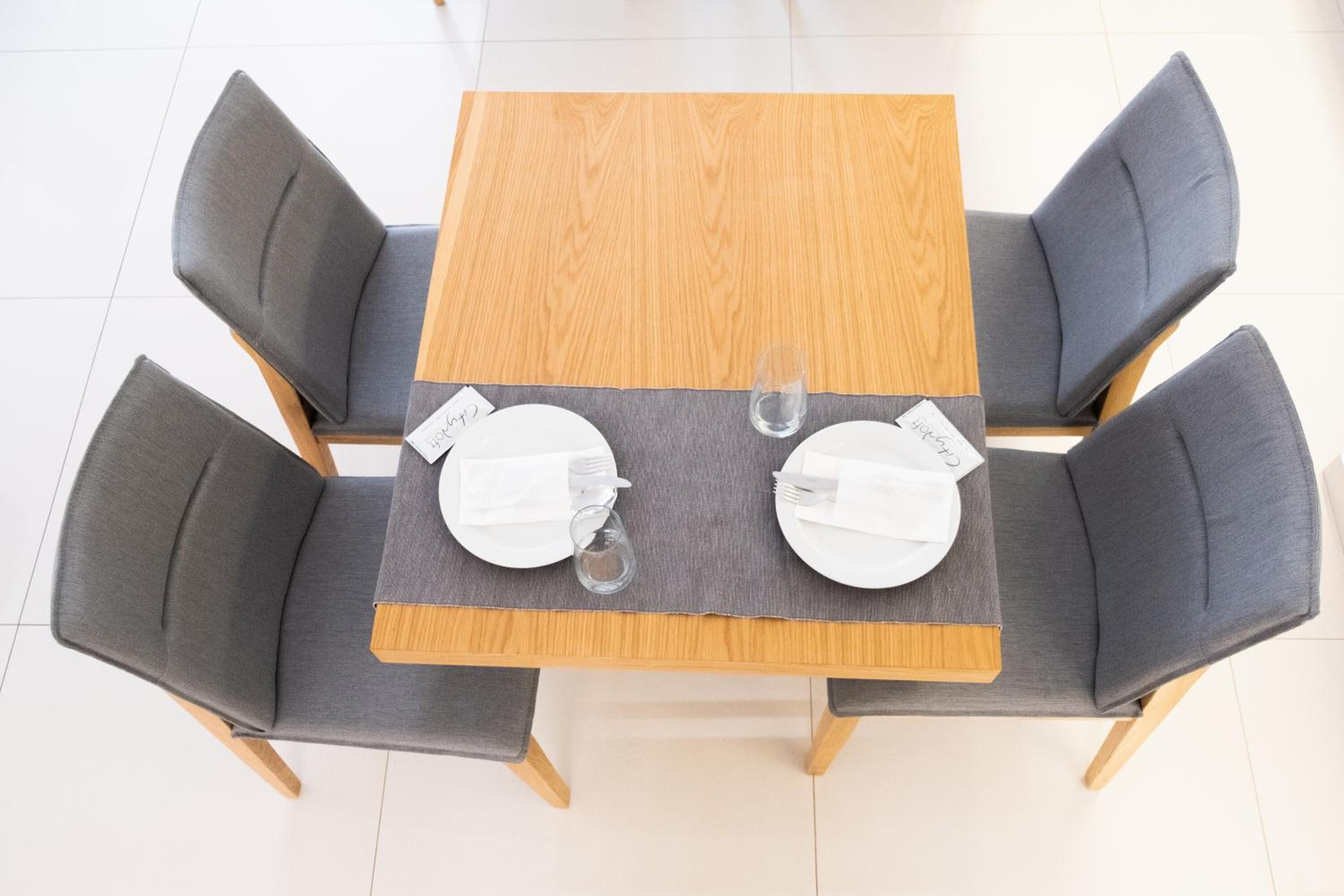 A square wooden table with a grey cloth, surrounded by four grey upholstered chairs.