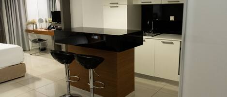 Una habitación de hotel moderna con área de cocina, una mesa de comedor con dos taburetes tipo barra, una cama y un espejo grande.