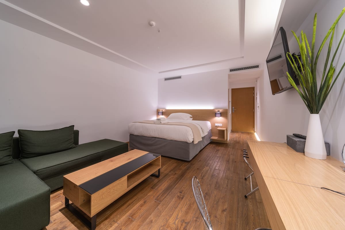 Ein modernes Hotelzimmer mit einem Bett, einem grünen Sofa, einem Holztisch und einer großen Topfpflanze.