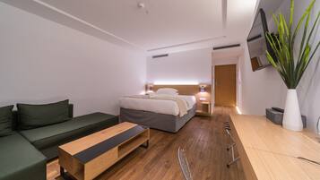 A modern hotel room with a bed, green sofa, wooden coffee table, and a large potted plant.