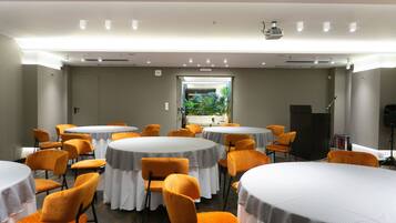 A conference room with multiple tables and chairs, a projector, and a window with a view of greenery.
