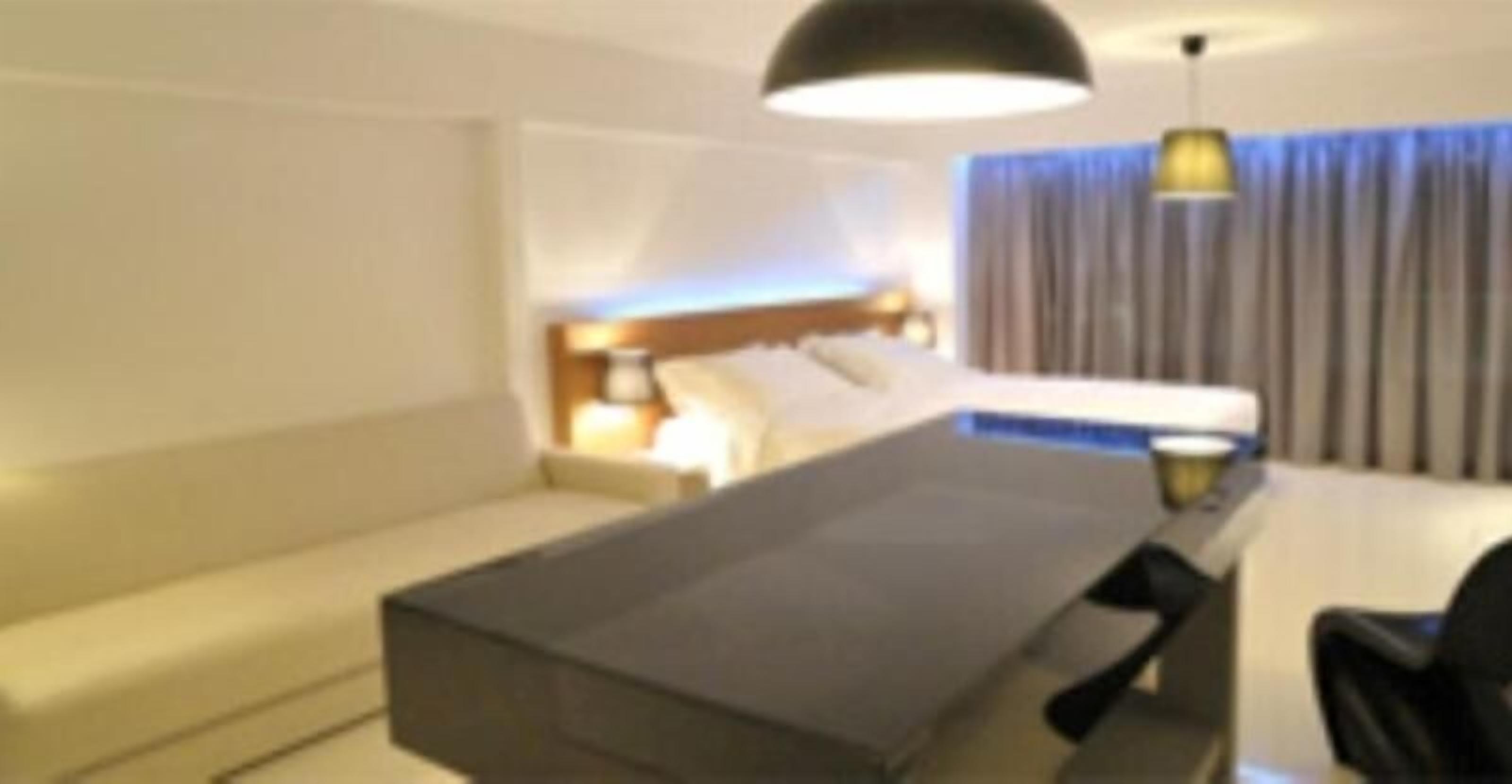 A hotel room with a bed, a sofa, a desk, and a lamp.