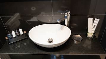 Uma casa de banho moderna com uma pia branca, torneira cromada e bancada preta.