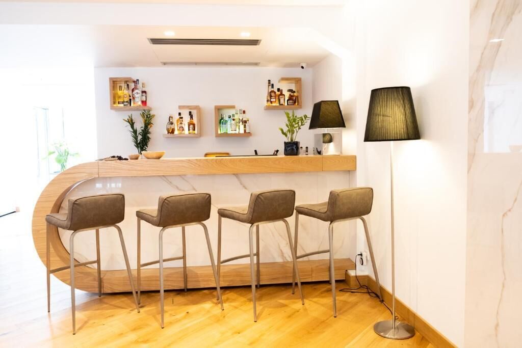 Un espace bar moderne avec un comptoir en bois incurvé, quatre tabourets de bar et un lampadaire.