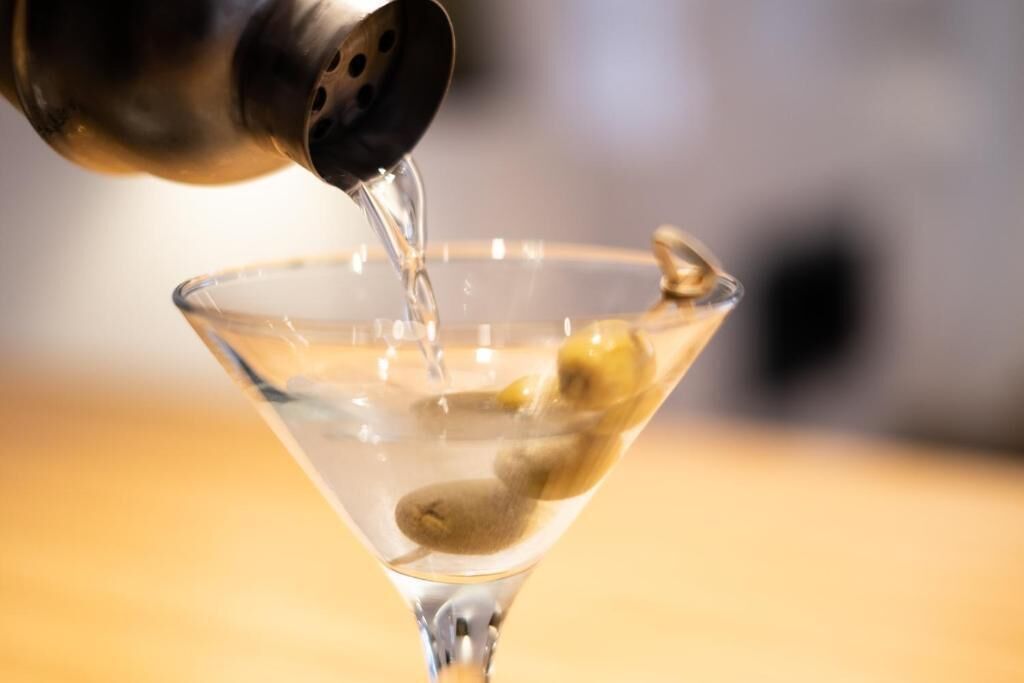 Een martini glas waar een heldere vloeistof in gegoten wordt.