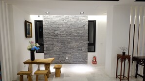 Un intérieur moderne avec un mur en pierre, une table à manger en bois avec des bancs, un vase de fleurs et, à droite, une table en bois traditionnelle.