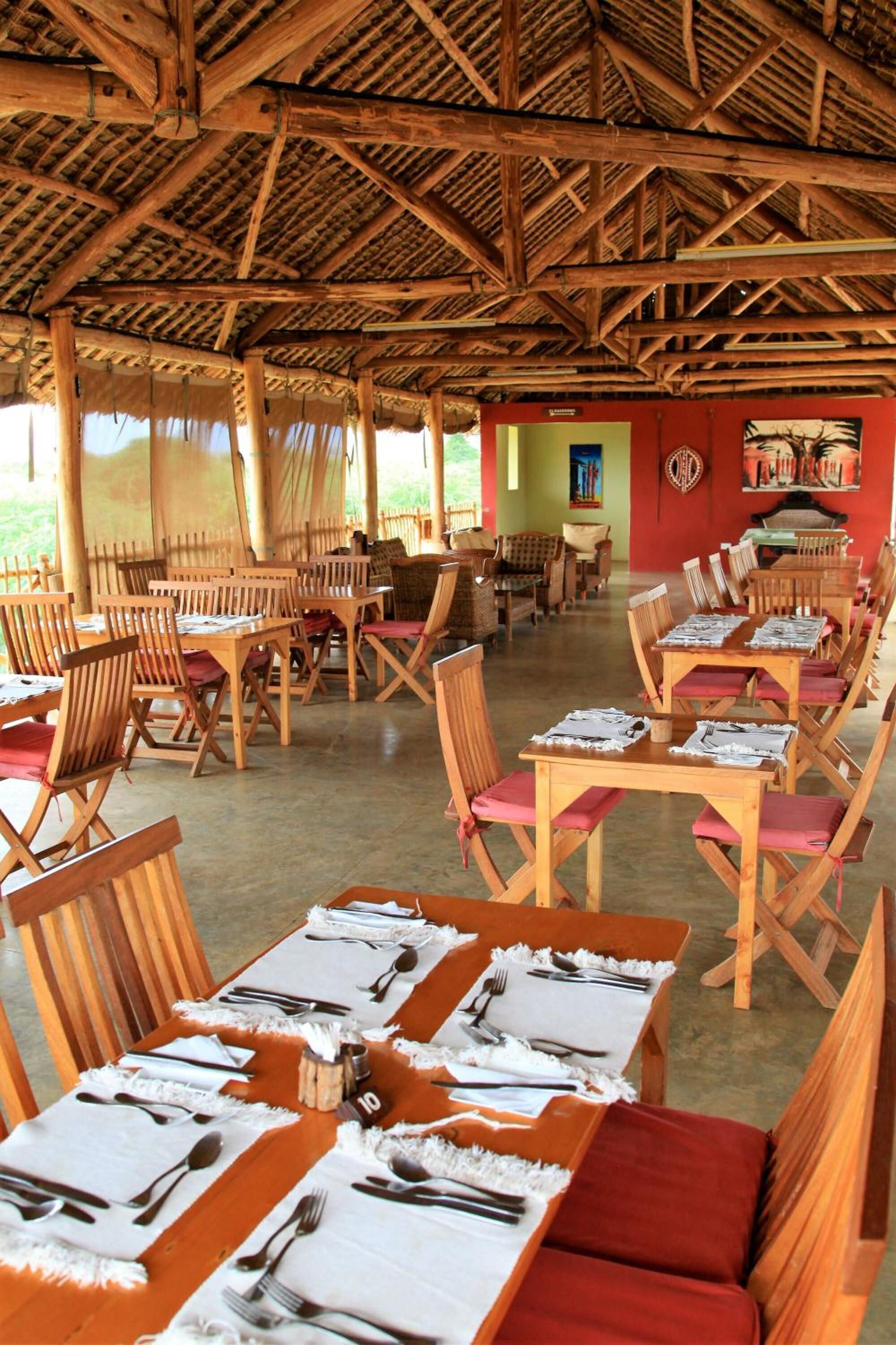 Un restaurante con mesas y sillas de madera, techo de paja y vistas al exterior.