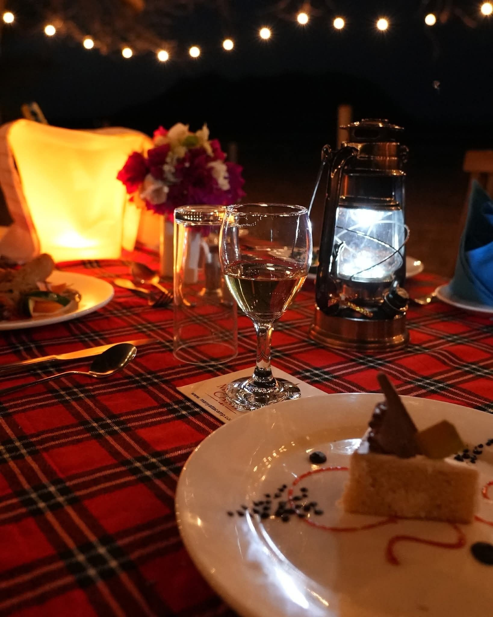 A dining table with a plaid tablecloth, a candle, a glass of wine, and a dessert plate.