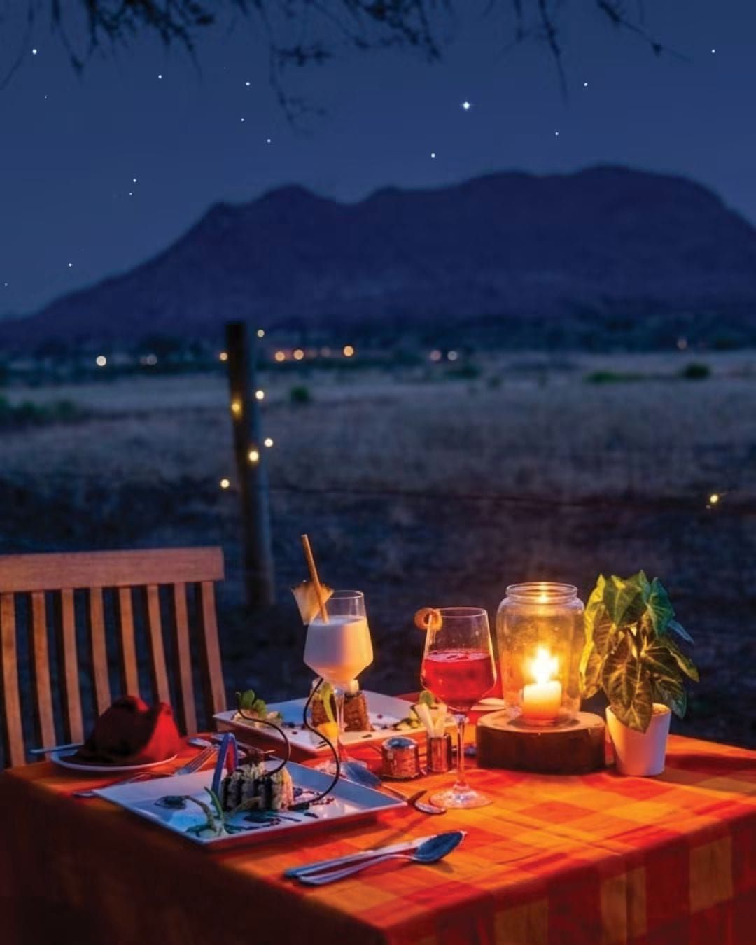 An outdoor dining setup with a table, chairs, and a candle, set against a mountainous backdrop.