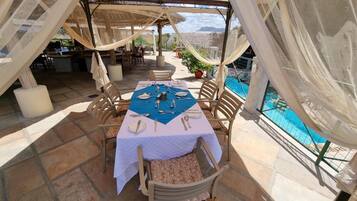 An outdoor dining area with a table set for two, overlooking a pool and a mountainous landscape.