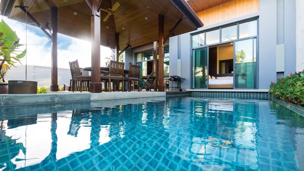 A modern pool area with tiled flooring, wooden furniture, and a covered seating area. - Onyx White Pearl Villa (Rawai)
