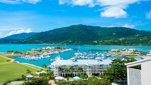 A marina with boats, a dock, and buildings with a view of the sea and a hill in the background. - Ocean Views 49A (Airlie Beach)