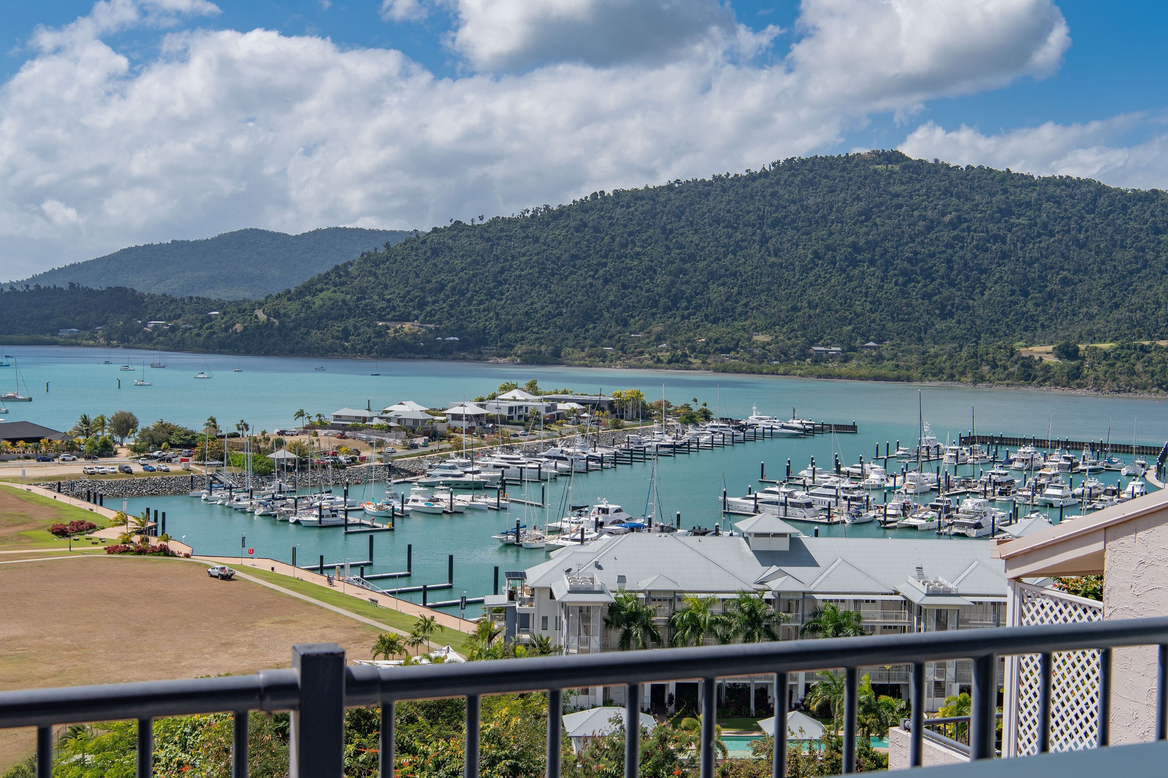 A marina with boats docked, surrounded by greenery and hills.