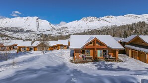Un paysage montagneux enneigé, avec des chalets en bois dotés de grandes fenêtres et d’une terrasse en bois.