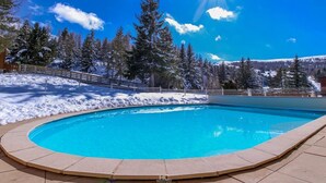 Une piscine d’eau cristalline, entourée d’arbres couverts de neige et bordée d’une clôture en bois.