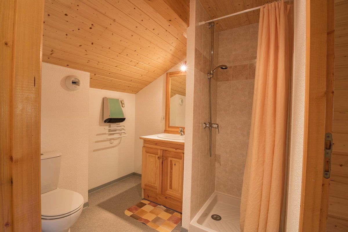 Et badeværelse med træpaneler, toilet, håndvask og brusebad.