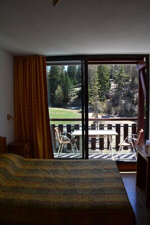 A bedroom with a large window, a bed, and a view of a deck and outdoor area. - Chalets Margot (Le Dévoluy)