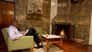 Un hombre leyendo en una habitación con chimenea de piedra, un sillón verde y una mesa de centro de madera.