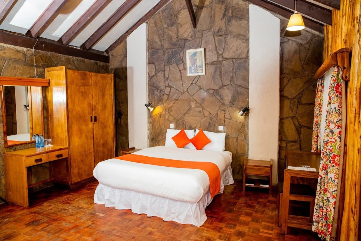 Un dormitorio con pared de piedra, muebles de madera, cama con almohadas anaranjadas y un escritorio de madera con espejo.