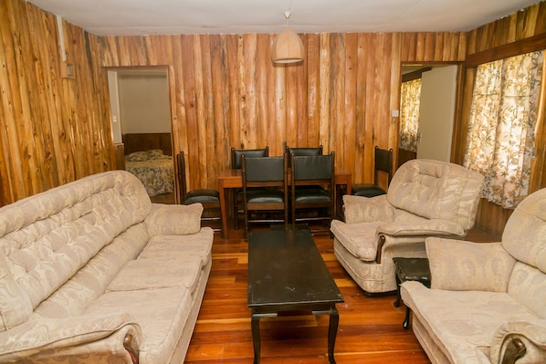 Una habitación con paredes de paneles de madera, un conjunto de sofás, una mesa de comedor con sillas y una lámpara colgante.