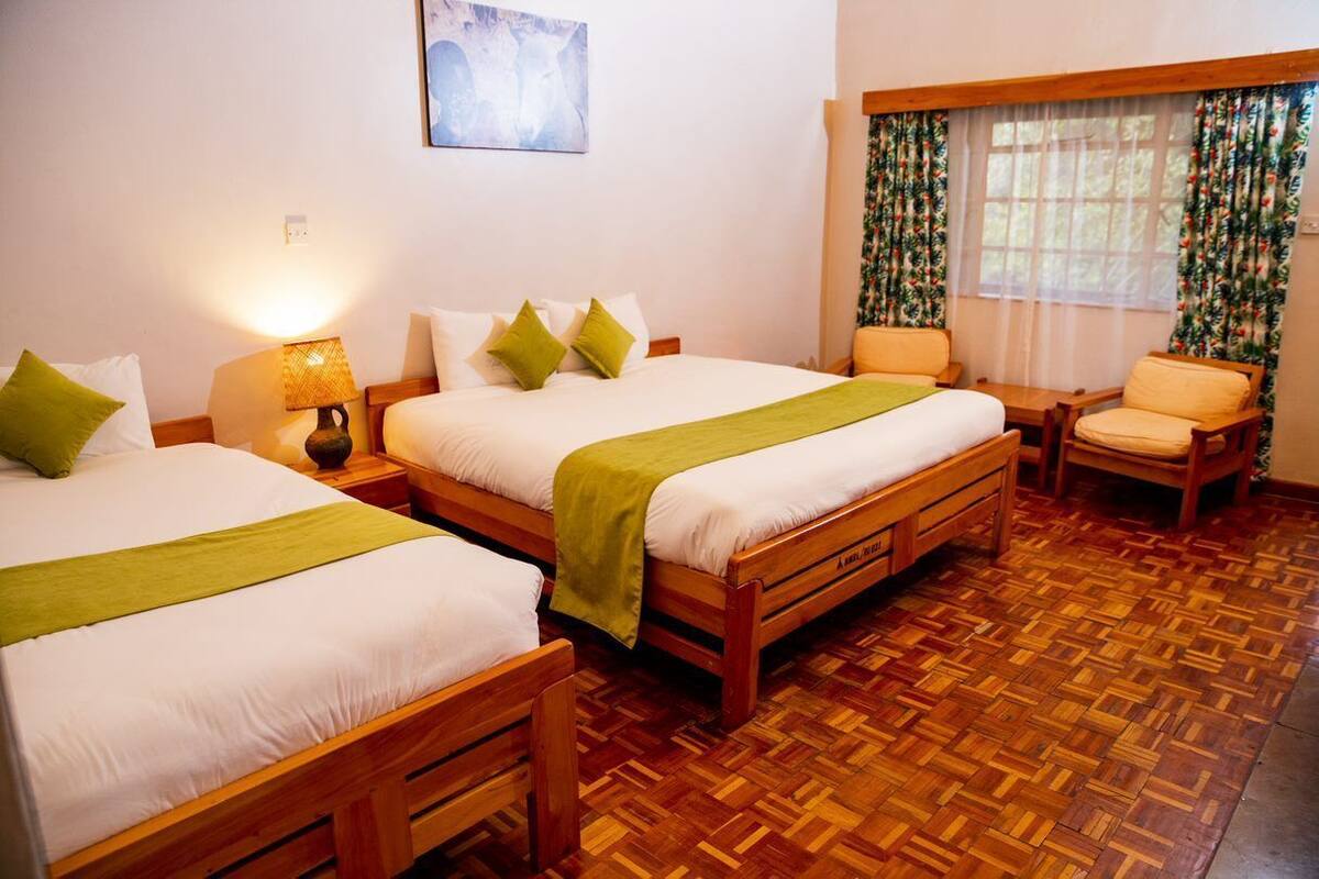 Habitación de hotel con dos camas de madera, una silla, una mesa y un ventanal con cortinas.