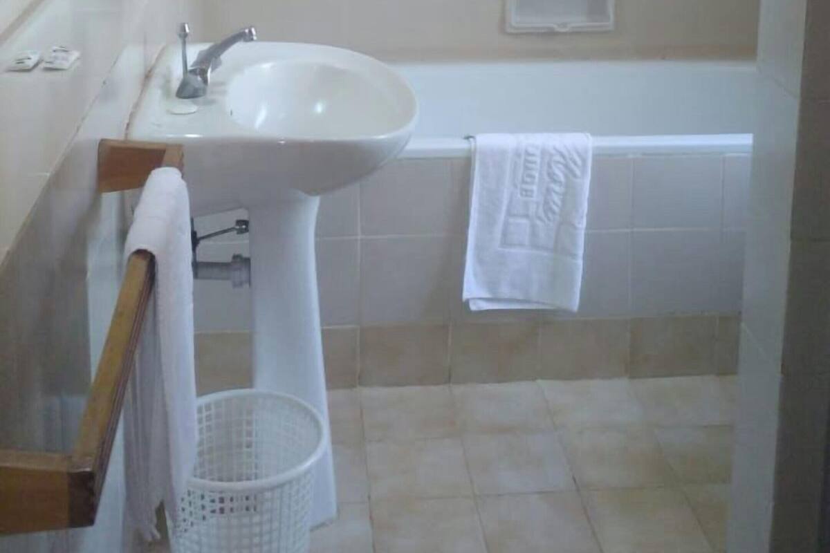 Un baño con lavamanos, espejo, toallero, bañera y cesta de ropa.
