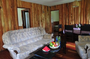 A room with a sofa, dining table, chairs, and a fruit bowl.