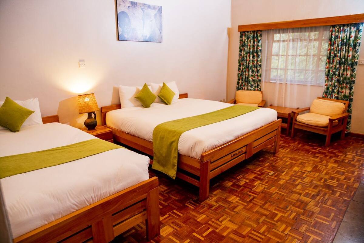 Habitación de hotel con dos camas de madera, una silla, una mesa y un ventanal con cortinas.