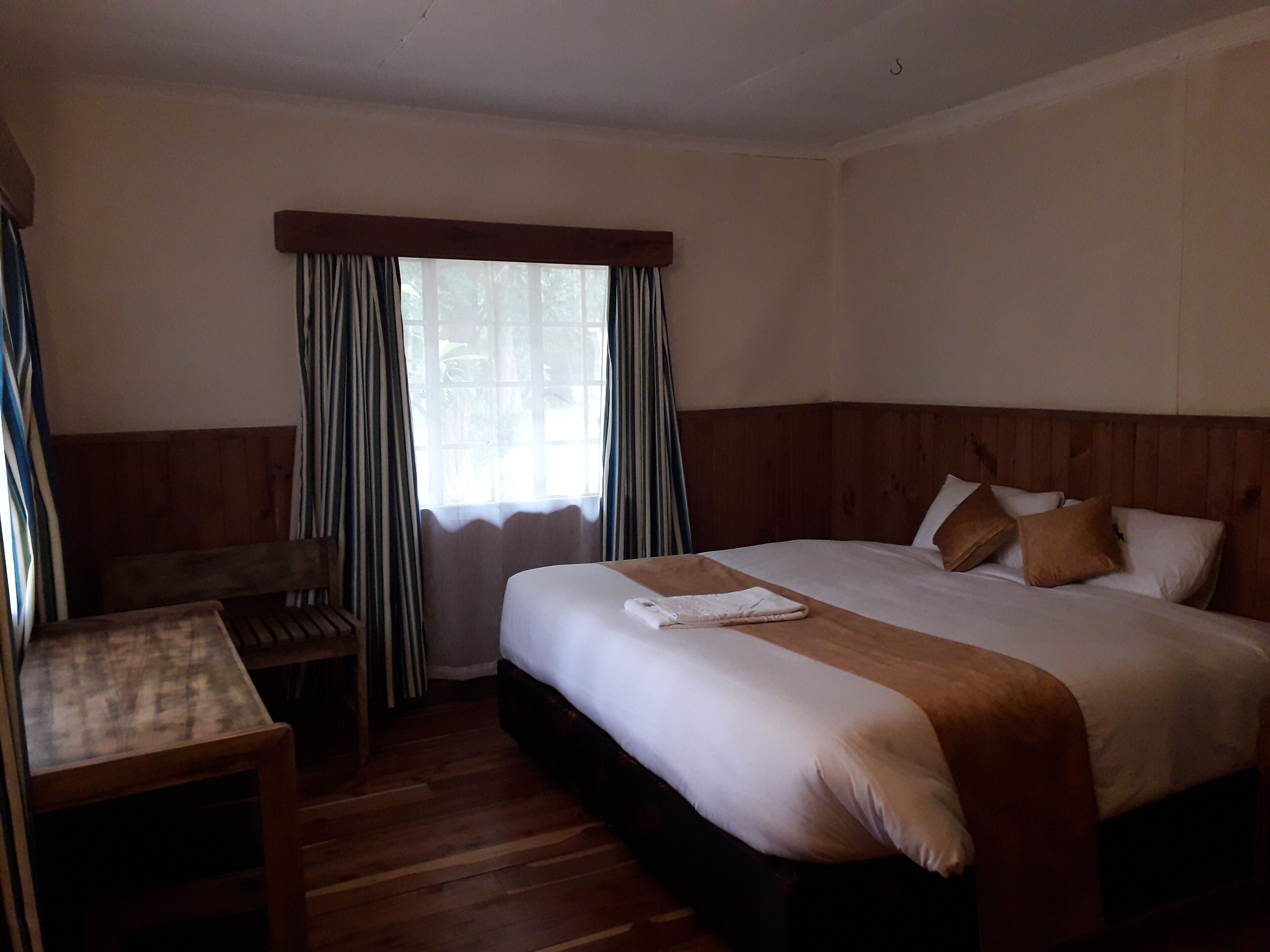 Een hotelkamer met een groot bed, een houten hoofdbord, een klein tafeltje en een raam met gordijnen.