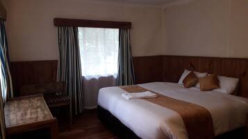 Een hotelkamer met een groot bed, een houten hoofdbord, een klein tafeltje en een raam met gordijnen.