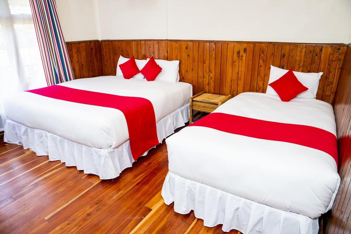 Dos camas dobles con ropa blanca y detalles en rojo, cabeceros de madera y suelo de madera.