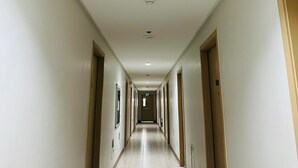 Un largo y estrecho pasillo de hotel con puertas a ambos lados, suelo de baldosas e iluminación empotrada en el techo.