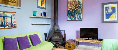 A cozy living room with a green sofa, a fireplace, a television, and various artworks on the walls.