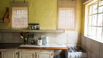 A kitchen with a gas stove, a microwave, and a toaster. There are wooden cabinets and a window with blinds.