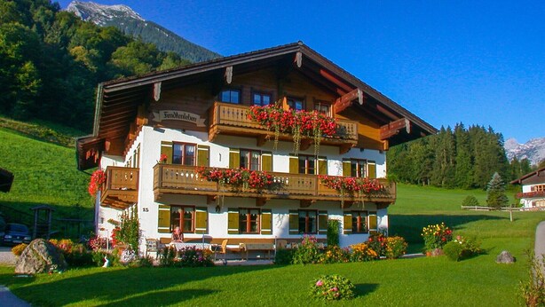 A traditional Alpine-style building with a balcony, surrounded by lush greenery and mountains in the background. - Ferienwohnung Taubensee, 1-2 Personen, 45 qm, Bad + Dusche/WC, Südbalkon, TV, 1 Schlafzimmer, Nichtraucher (Ramsau bei Berchtesgaden)