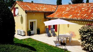 A yellow building with a tiled roof, a patio with outdoor furniture, and a satellite dish. - Gîtes La Bakénia (Villeneuve-sur-Lot)
