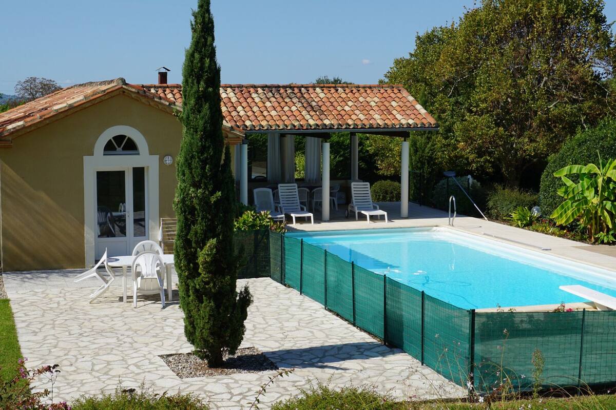 A poolside area with a covered seating area, a pool, and a small building with a door.