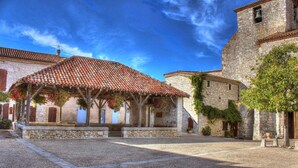 A courtyard with a covered seating area, stone buildings, and a bell tower. - Gîtes La Bakénia (Villeneuve-sur-Lot)