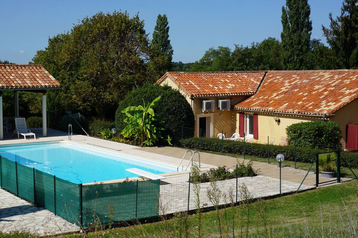 A swimming pool with a tiled deck, surrounded by a fence, and adjacent to a building with a tiled roof.