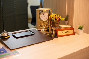 A reception desk with a clock, a nameplate, a small plant, and a vase with flowers. - Naha Lagoon Hotel I (Naha)