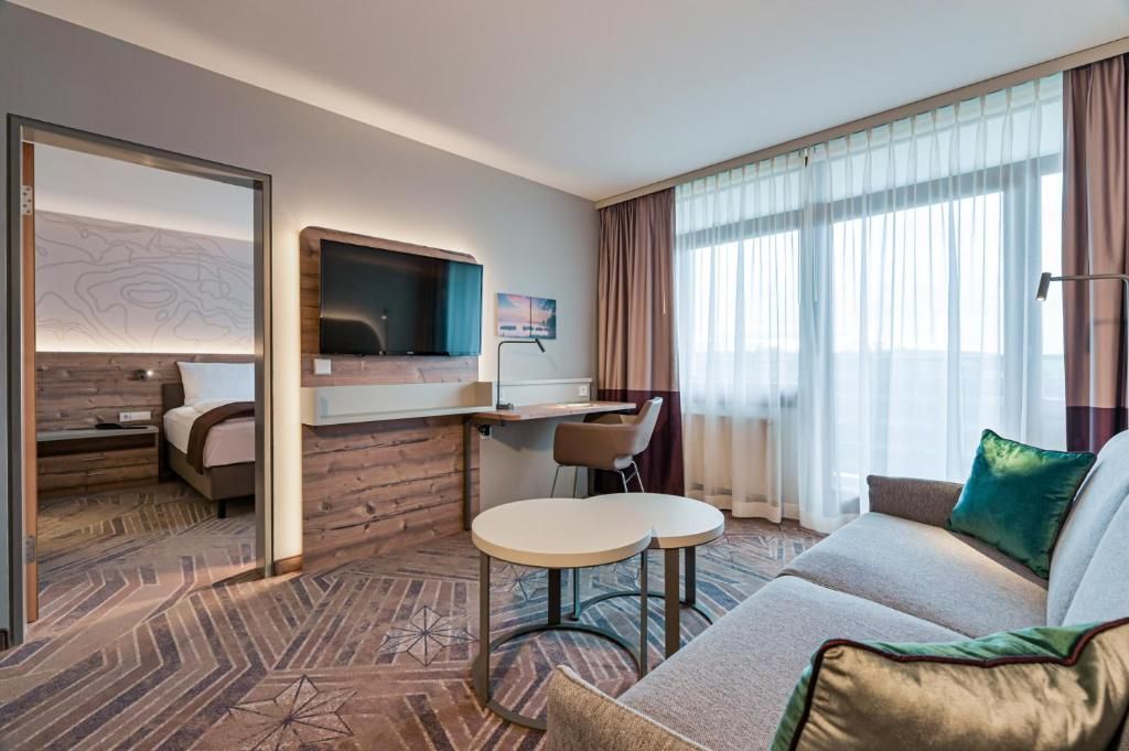 Ein Hotelzimmer mit Bett, Schreibtisch mit Stuhl, Sofa und Fernseher.