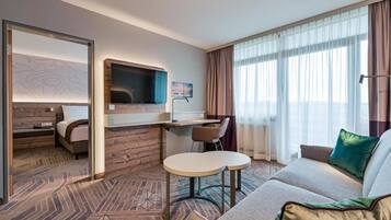 Ein Hotelzimmer mit Bett, Schreibtisch mit Stuhl, Sofa und Fernseher.