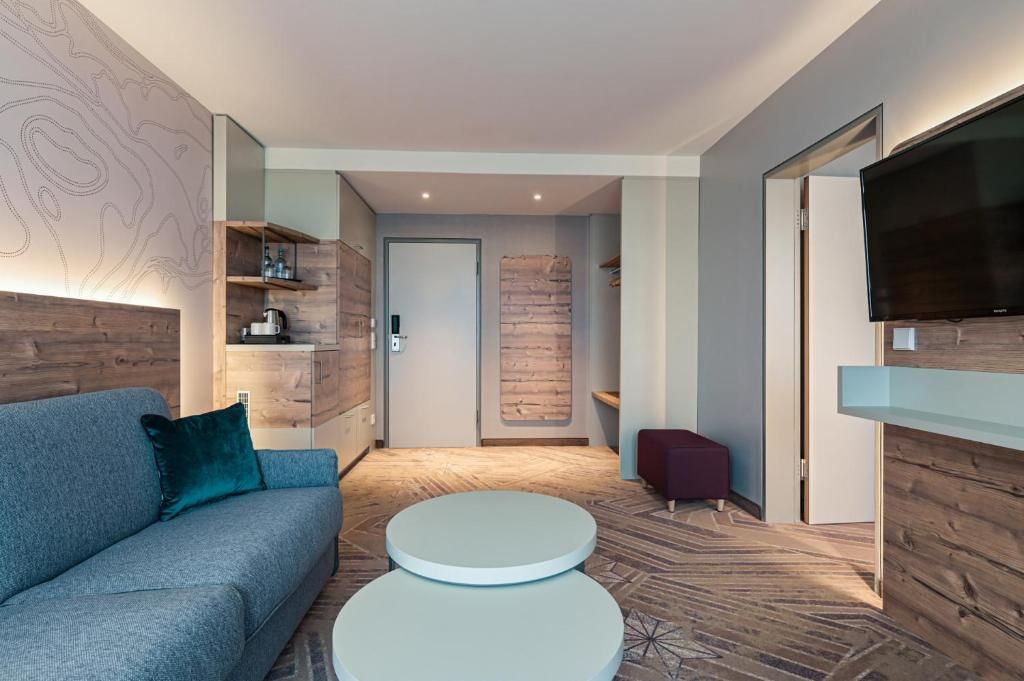 A modern living room with a sofa, a coffee table, a flat-screen TV mounted on a wooden wall, and a patterned floor.