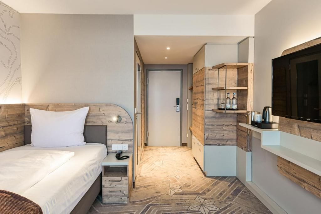 Ein Hotelzimmer mit Bett, Fernseher, einer Küchenzeile und einer Tür zu einem anderen Raum.