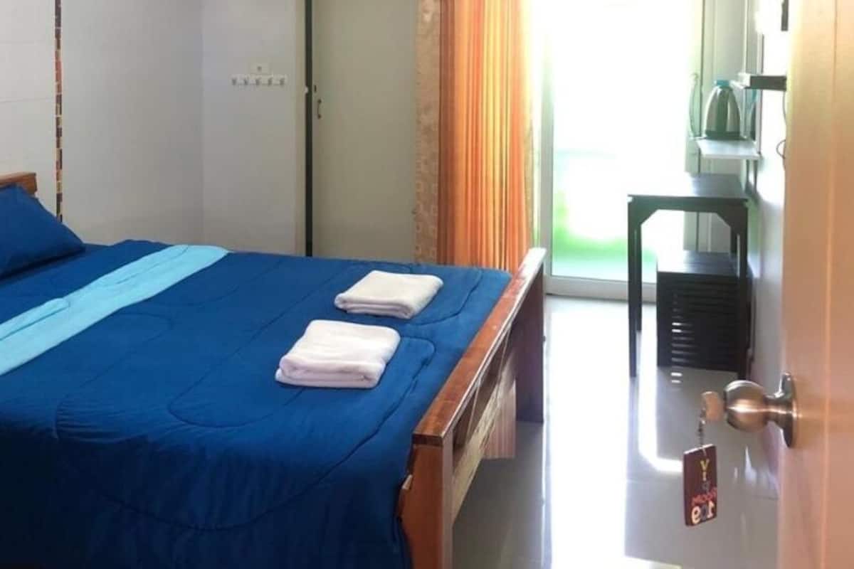 A hotel room with a bed, two pillows, a blue bedspread, two folded towels, a small table, and a door with a keychain.