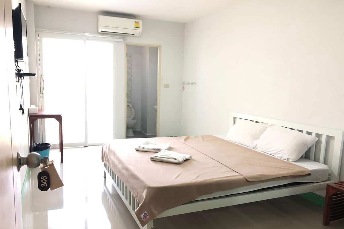 A bedroom with a bed, a door, an air conditioning unit, and a view of the outside.