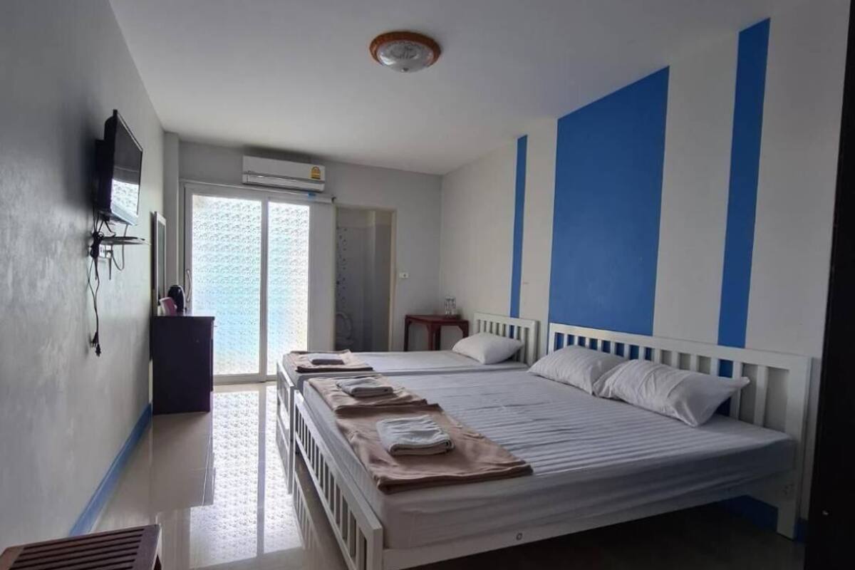 A bedroom with a large bed, a TV mounted on the wall, a desk, and a window with a view.